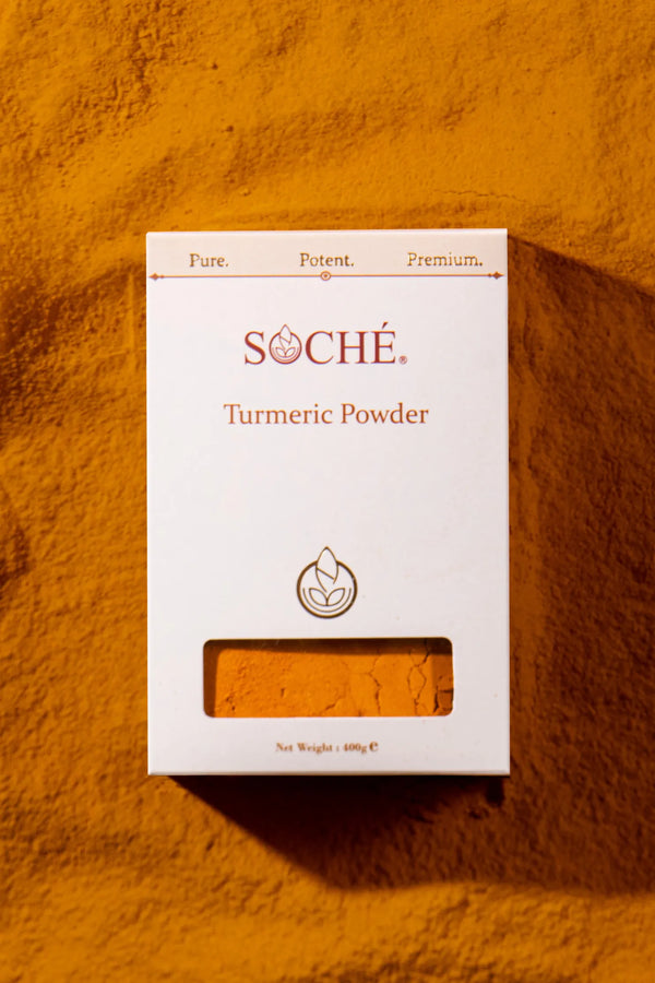 A white box of Soché Turmeric Powder with a clear window showing the orange-yellow powder inside, set against a textured orange-yellow background.